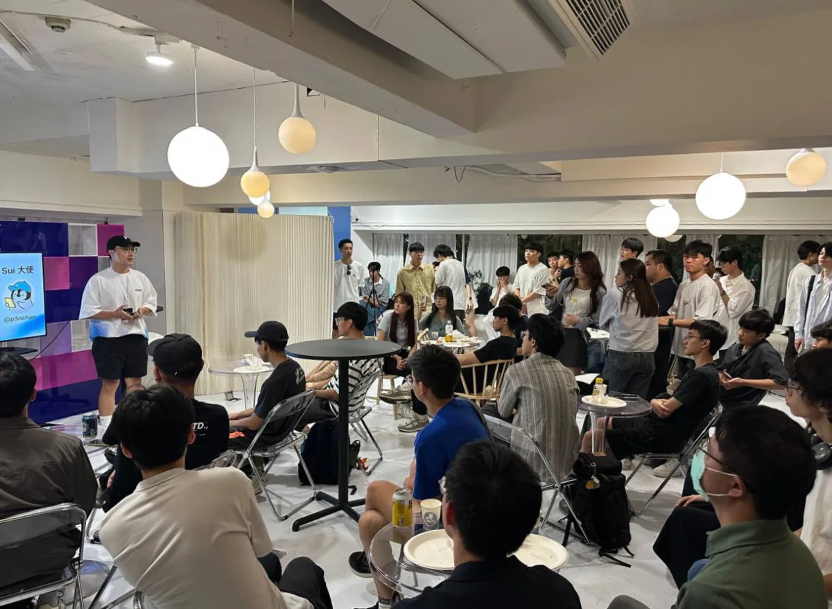 Penchan sharing experiences with Sui and AI at an indoor event, with a full audience of students.